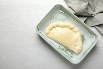 Uncooked calzone pizza in baking dish on white wooden table, top view. Space for text