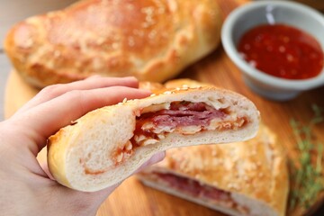 Woman with piece of calzone pizza at wooden table, closeup
