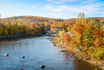 Arch road bridge spanning a river  in a forested hilly landscape at the peak of autumn colours on a...