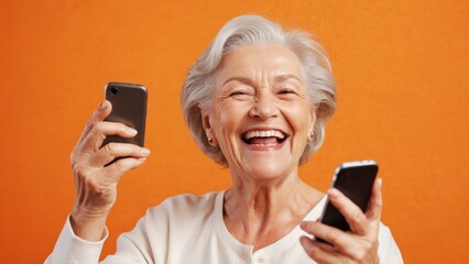 Fototapeta premium Joyful senior woman laughing while using her smartphone against a bright orange background