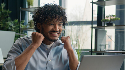 Amazed excited Arabian Indian latin man celebrate business achievement in office winning project on...