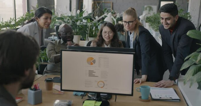 Multiethnic group of businesspeople making online video call looking at computer screen talking standing in office. Virtual meeting and professional communication concept.
