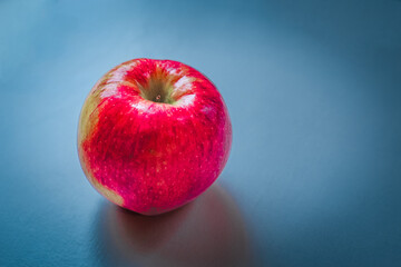 abstract large juicy red smooth reflective apple with texture and extra shine with soft blue cloudy background for creative design projects