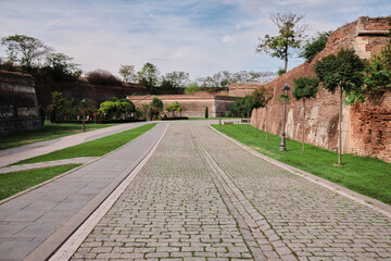 Cobblestone path winds through a historic park, flanked by ancient brick walls and lush greenery.  A serene and picturesque scene perfect for travel or historical contexts.
