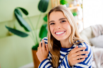 Fototapeta premium Photo of nice blonde young girl hugging self touch shoulder wear striped clothes enjoy modern cozy interior flat indoors