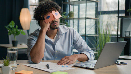 Funny lazy businessman tired male business manager napping at office desk Arabian Indian man sleep...