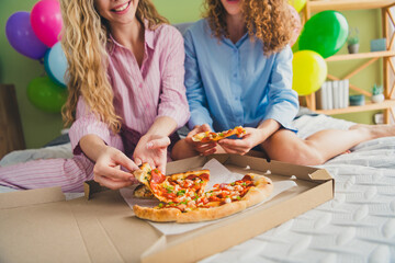 Cropped full size photo of two attractive young women eating pizza sit bed dressed sleepwear outfit wake up day light bedroom home interior