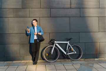 Man standing by a wall with a bicycle while checking his phone in an urban setting