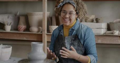 Portrait of creative influencer recording video about pottery in workshop talking and making pot. Joyful vlogger having fun with clay and speaking then waving hand.