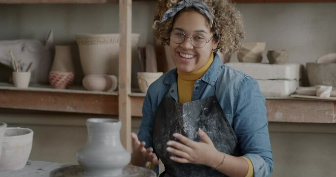 Portrait of creative influencer recording video about pottery in workshop talking and making pot. Joyful vlogger having fun with clay and speaking then waving hand.
