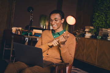 Young man in casual cardigan studying on laptop at home in evening ambient setting