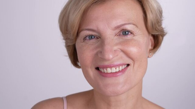 Blond mature woman plays with a cotton pad while posing for a portrait. Modern skincare practices for wrinkle prevention and natural beauty