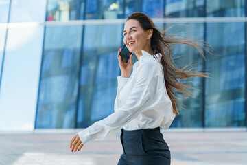 Young professional woman talks on phone while walking outside modern office building in city