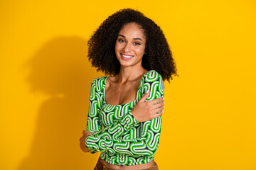 Charming young woman with curly hair in green top posing confidently with a happy smile against a vibrant yellow backdrop