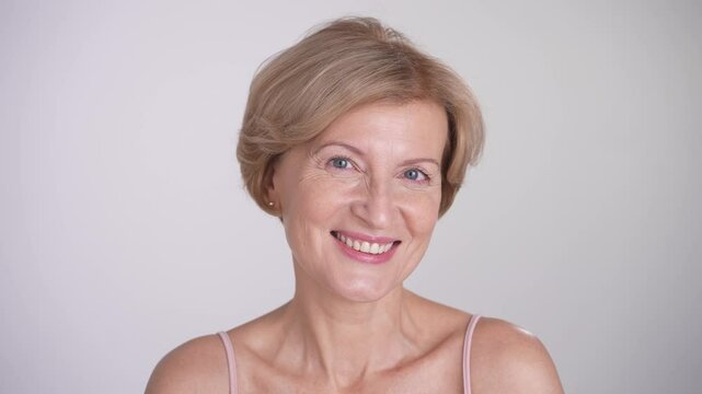 Pretty blond mature woman looking at camera and smiling. Beauty skincare and anti-aging facial care. Portrait on white background.