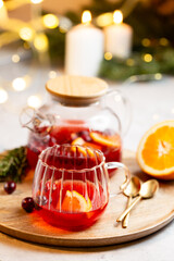 Natural home made tea with cranberry in a glass teapot, served with oranges and rosemary on a christmas background