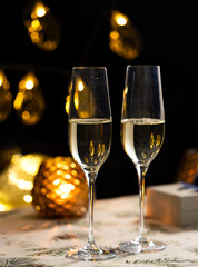 concept of celebrating christmas and new year, two glasses of champagne on the background of candles and colorful garlands, warm home traditional festive atmosphere