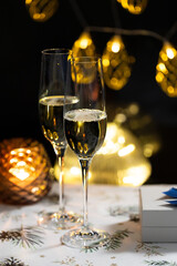 concept of celebrating christmas and new year, two glasses of champagne on the background of candles and colorful garlands, warm home traditional festive atmosphere