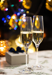 concept of celebrating christmas and new year, two glasses of champagne on the background of candles and colorful garlands, warm home traditional festive atmosphere