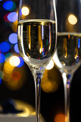 concept of celebrating christmas and new year, two glasses of champagne on the background of candles and colorful garlands, warm home traditional festive atmosphere