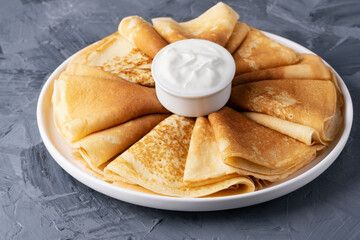 Stack of traditional russian pancakes blini with sour cream on gray background