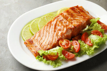 Delicious grilled salmon fillet with vegetable salad and lime on grey table, closeup
