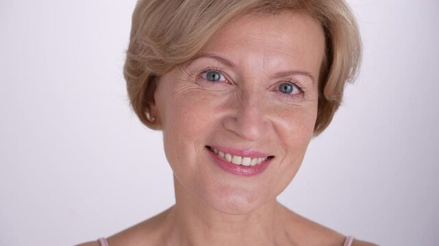 A portrait of a mature woman smiling confidently at camera. Beautiful blond female aging gracefully, using modern anti-aging skincare. 4k
