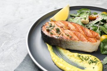 Tasty grilled salmon steak with lemon, sauce and salad on grey textured table, closeup. Space for text