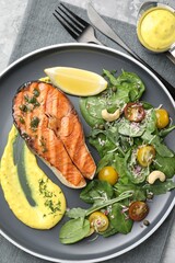 Tasty grilled salmon steak with sauce and salad on table, top view