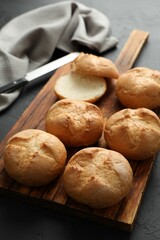 Board with homemade tasty buns on black textured table, closeup