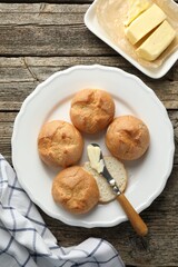 Plate with homemade tasty buns, butter and knife on wooden table, flat lay