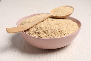 Oat bran in bowl and spoon on light wooden table, closeup