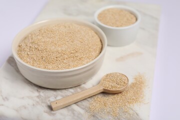 Oat bran in bowls and spoon on white table, closeup