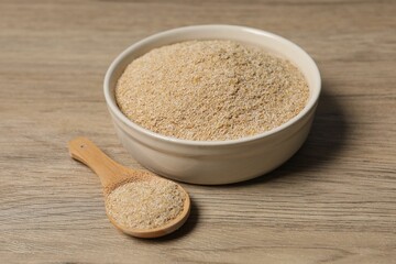 Oat bran in bowl and spoon on wooden table, closeup