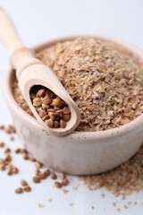Buckwheat bran in bowl and grains on white table, closeup