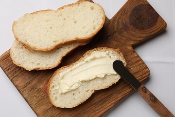 Fresh bread with butter and knife on white tiled table, top view