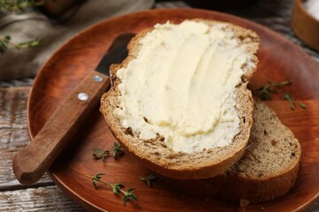 Fresh bread with butter and knife on wooden table, closeup
