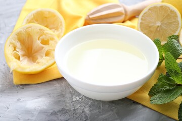 Fresh lemon juice in bowl, fruits, mint and squeezer on grey table, closeup