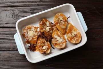 Delicious pears with caramel sauce, almond flakes and anise stars in baking dish on wooden table, top view