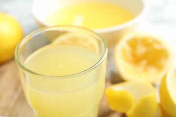 Glass of fresh lemon juice and squeezed fruits on table, closeup