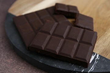 Pieces of delicious dark chocolate on brown table, closeup