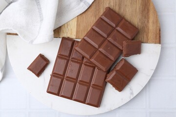 Pieces of delicious milk chocolate on white tiled table, top view