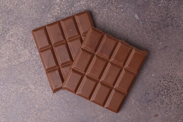 Pieces of delicious milk chocolate on brown table, top view