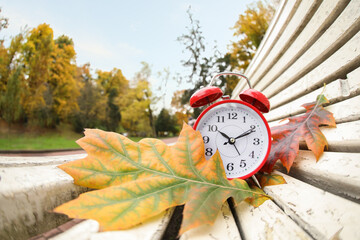 Autumn time. Alarm clock and fallen leaves on bench in park, wide angle lens