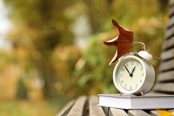 Autumn time. Alarm clock and book on bench in park, closeup. Space for text