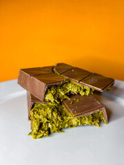 On an orange background, pieces of Dubai chocolate lie on a plate