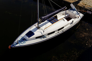 Yacht moored at marina pier. Boat tied with a rope. Sailboat docked. Top view of boat at the marina. Bow of the boat facing the water. Fastened at the dockside. Parked boat on a lake.