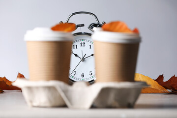Alarm clock, dry leaves and cups of coffee on light grey background, closeup