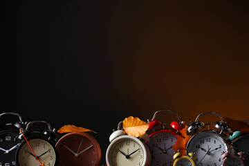 Alarm clocks and dry leaves on brown background, space for text