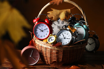 Alarm clocks and dry leaves in wicker basket on wooden table against brown background